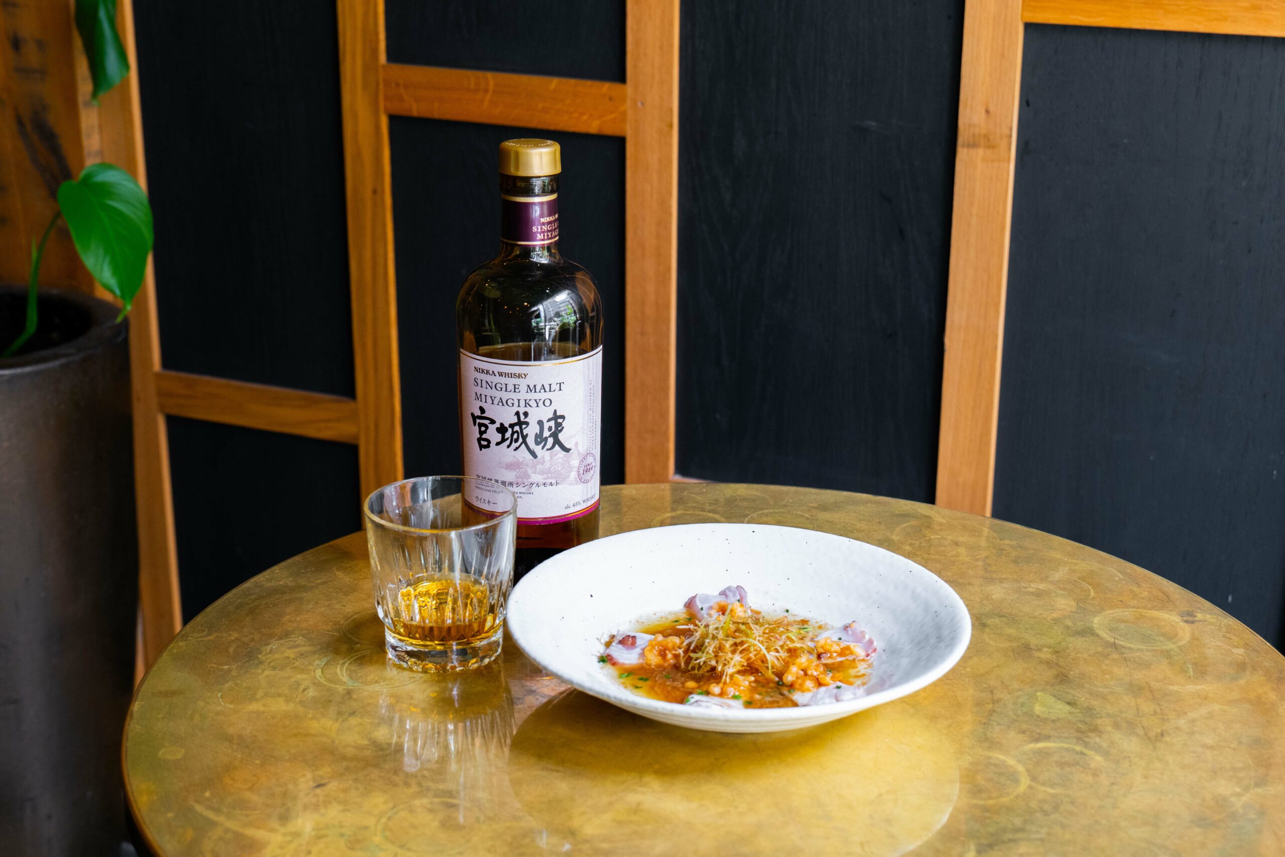 Nikka Whiskey, a glass of whiskey, and a plate with a meal on a gold table.