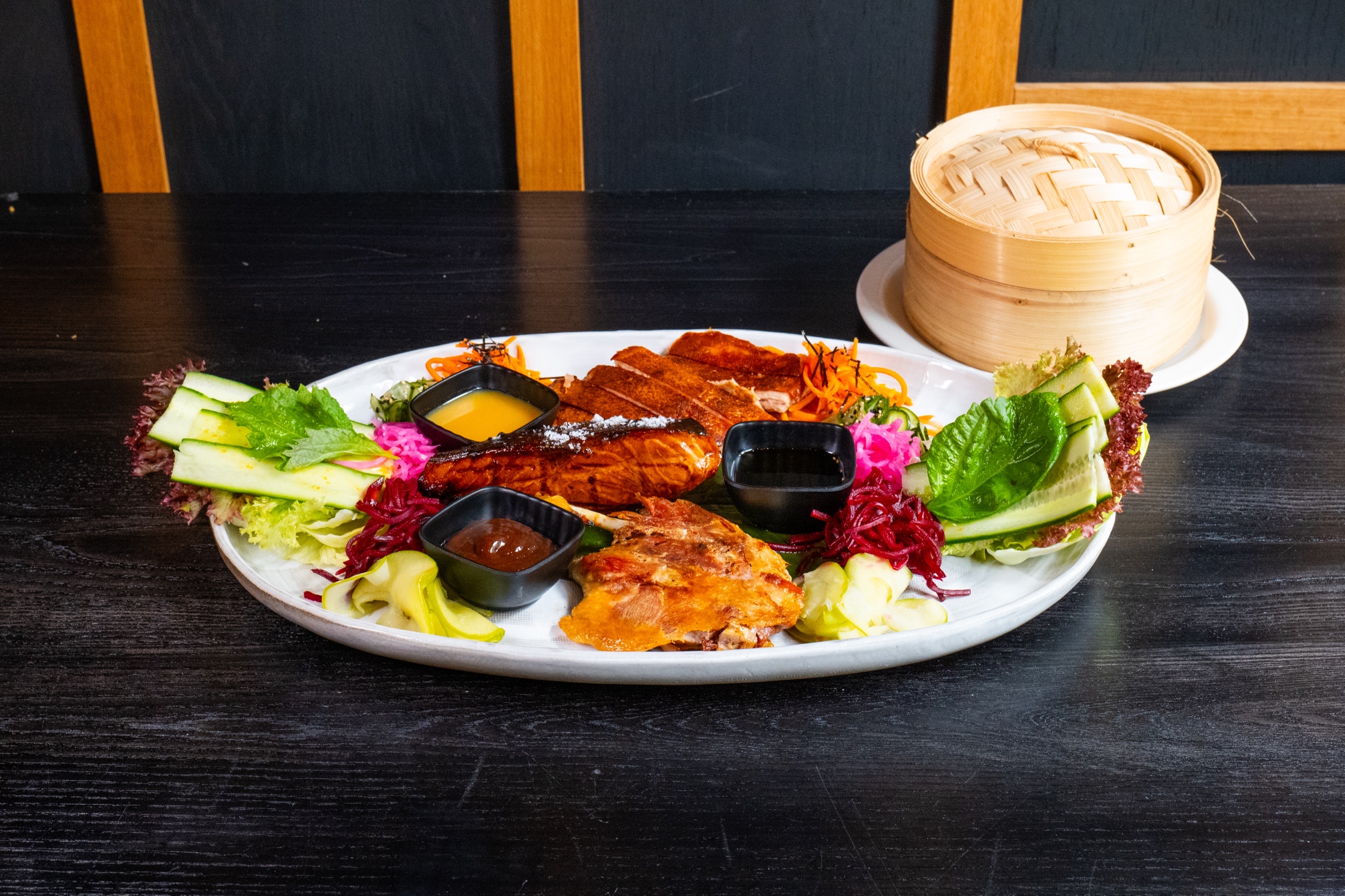 Gourmet duck and salmon dish plated with assorted vegetables on a white plate, with bamboo steamer basket.
