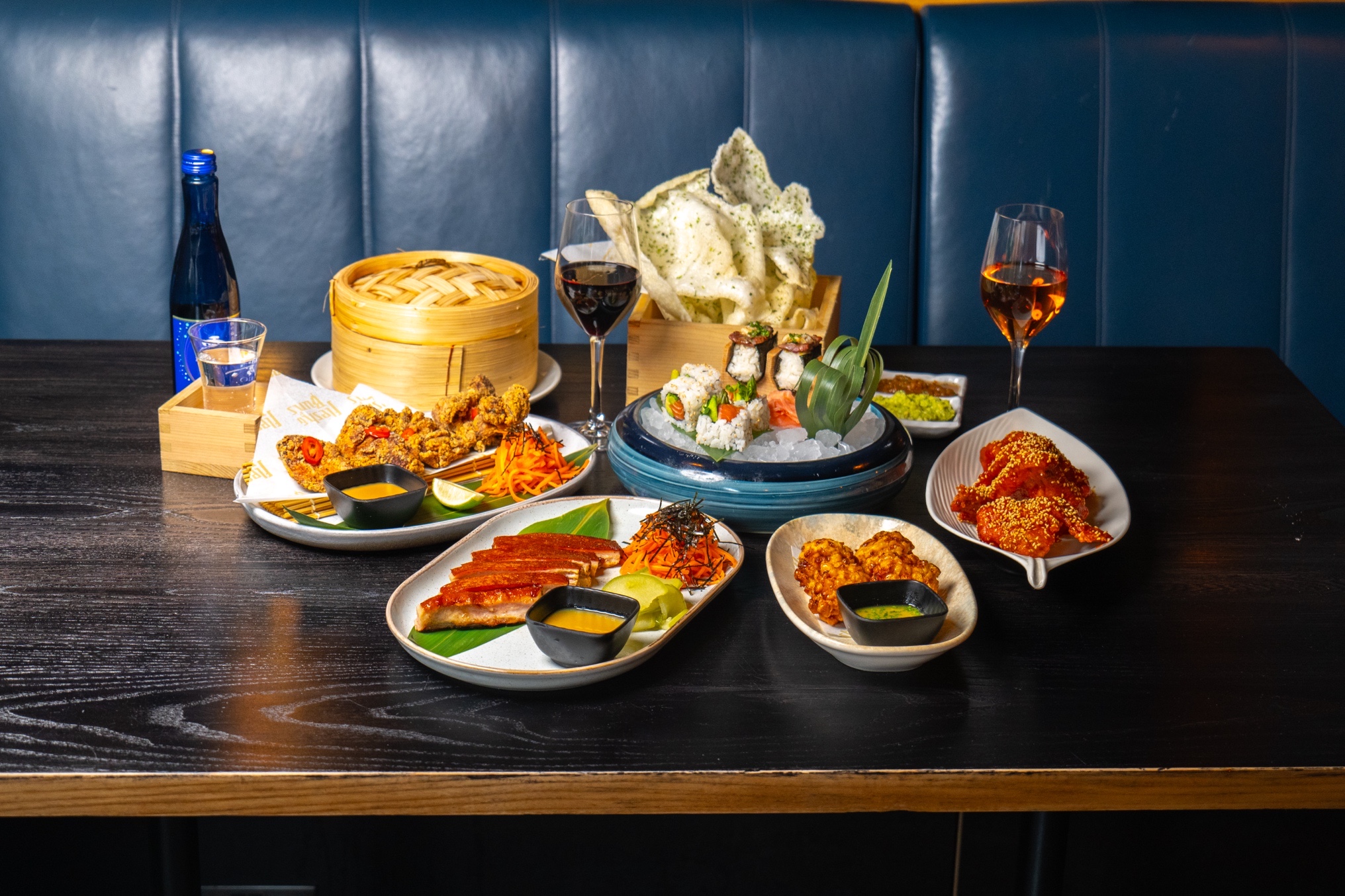 Assorted Asian cuisine spread on a black wooden table, including sushi, fried dishes, and beverages.