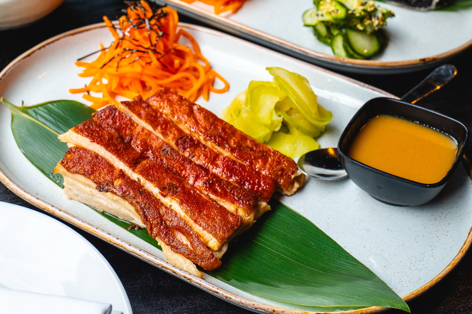Sliced crispy pork belly dish with sauce, carrots, and pickled vegetables on an oval plate.