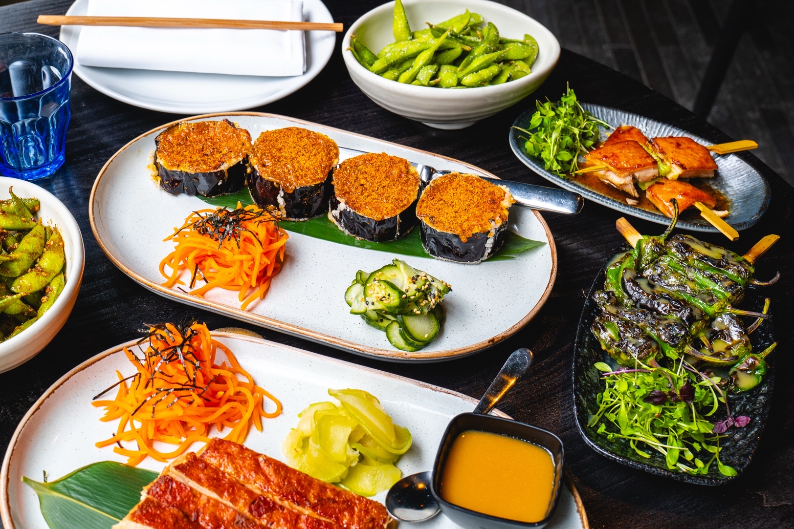 Assortment of Japanese appetizers: eggplant, edamame, chicken skewers, Shishito peppers, carrots, and pickles.
